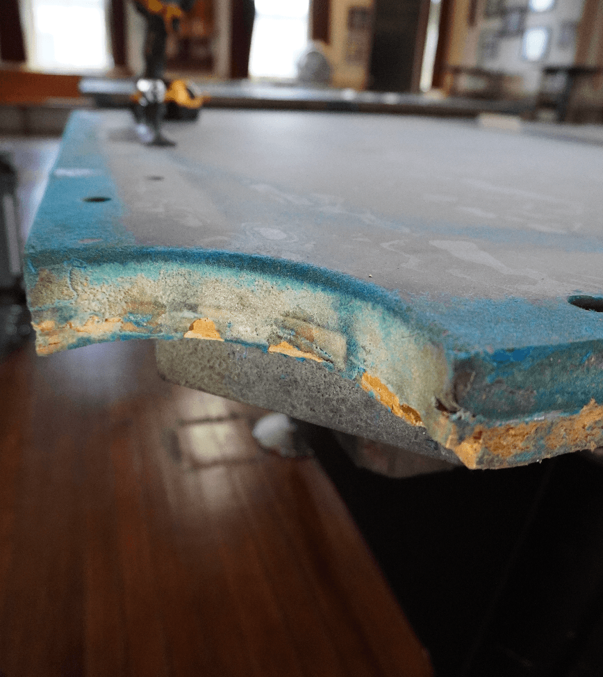 Pool table slate with crumbling, uneven seam filler and exposed particleboard from poor workmanship