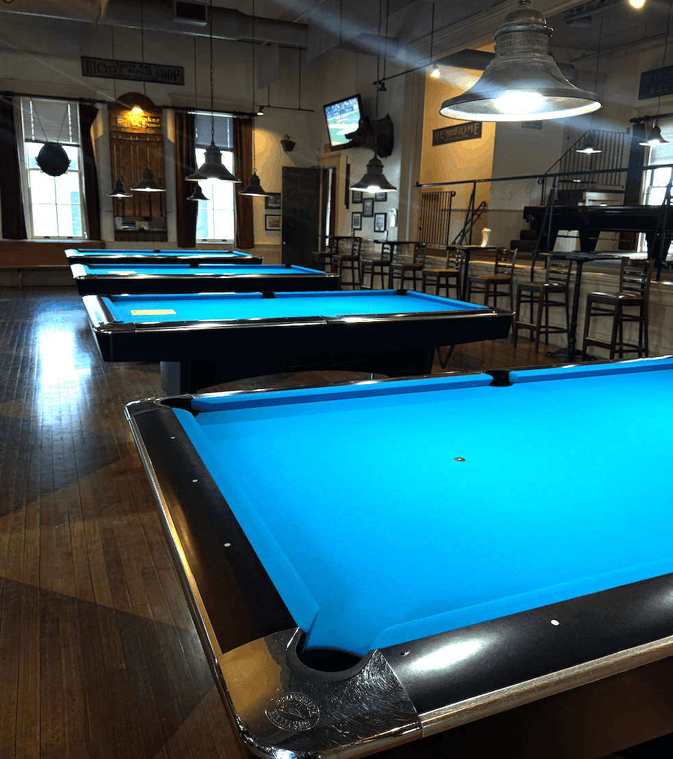 Row of chrome-railed tables with bright blue cloth in a pool hall