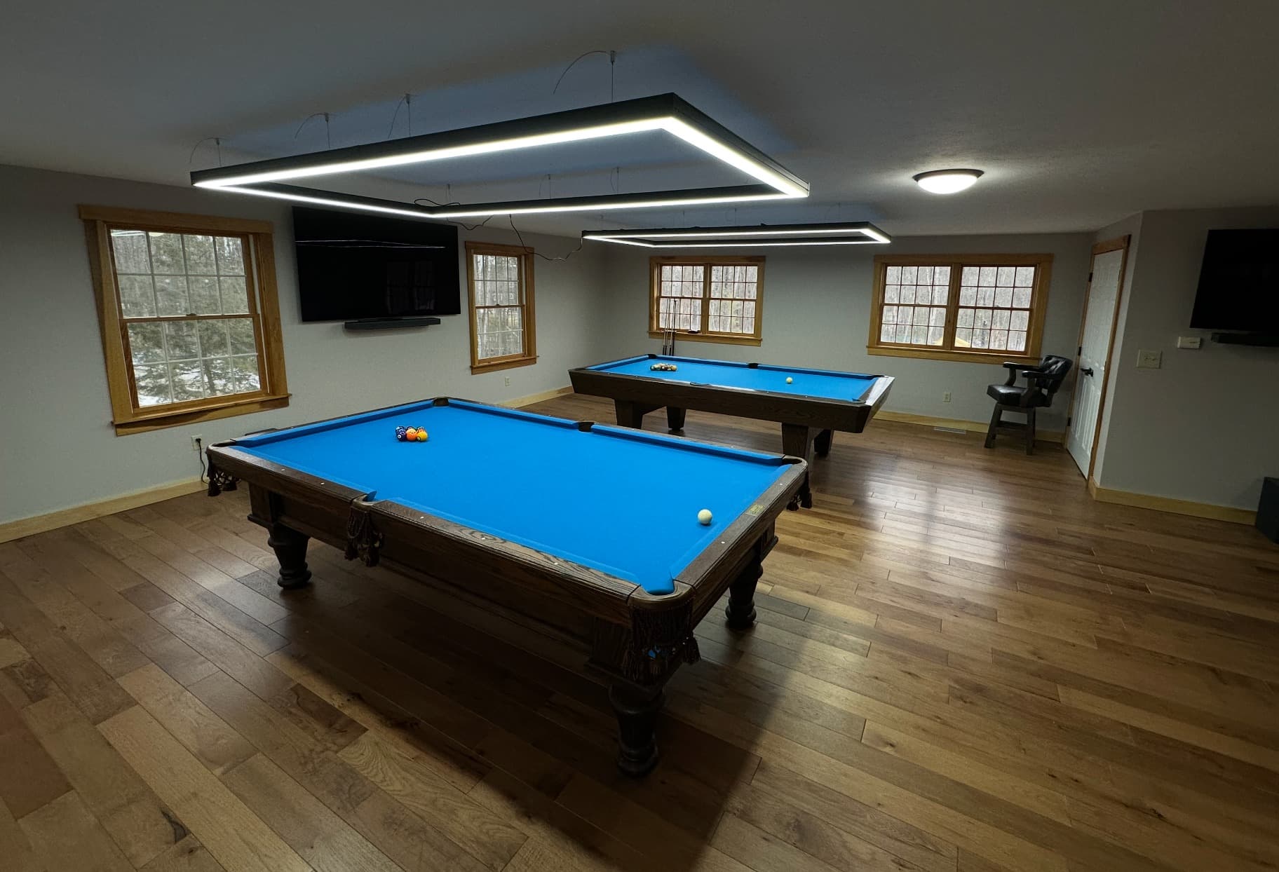 Finished basement game room with two blue-cloth pool tables under modern LED ring lights