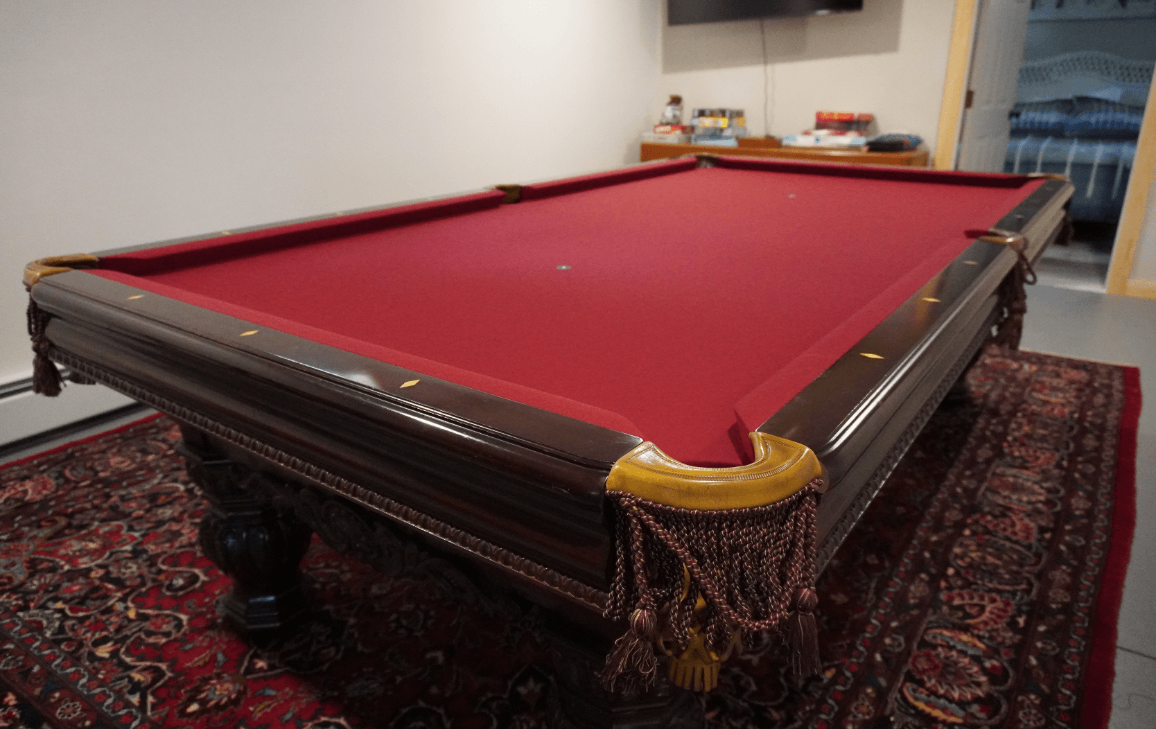 Antique carved pool table with burgundy cloth and fringed leather pockets on an oriental rug