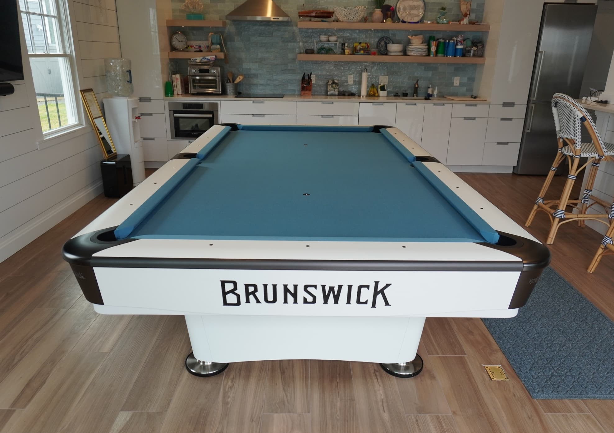 Front view of a white Brunswick pool table with blue cloth in a modern kitchen game room