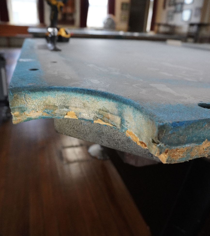 Pool table slate with crumbling, uneven seam filler and exposed particleboard from poor workmanship