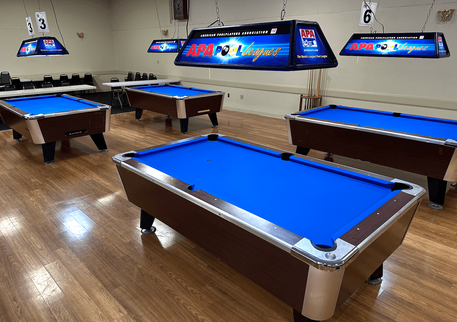 APA Pool Leagues room with multiple blue-felt tables