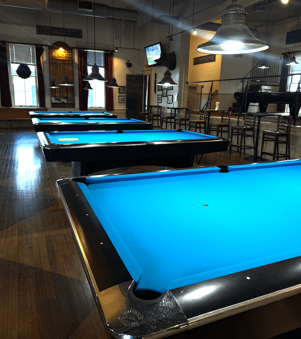 Row of chrome-railed tables with bright blue cloth in a pool hall